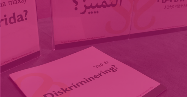 Vad är diskriminering rosa En broschyr med rubriken Vad är diskriminering? I bakgrunden syns fler broschyrer med samma rubrik fast på somaliska och arabiska.