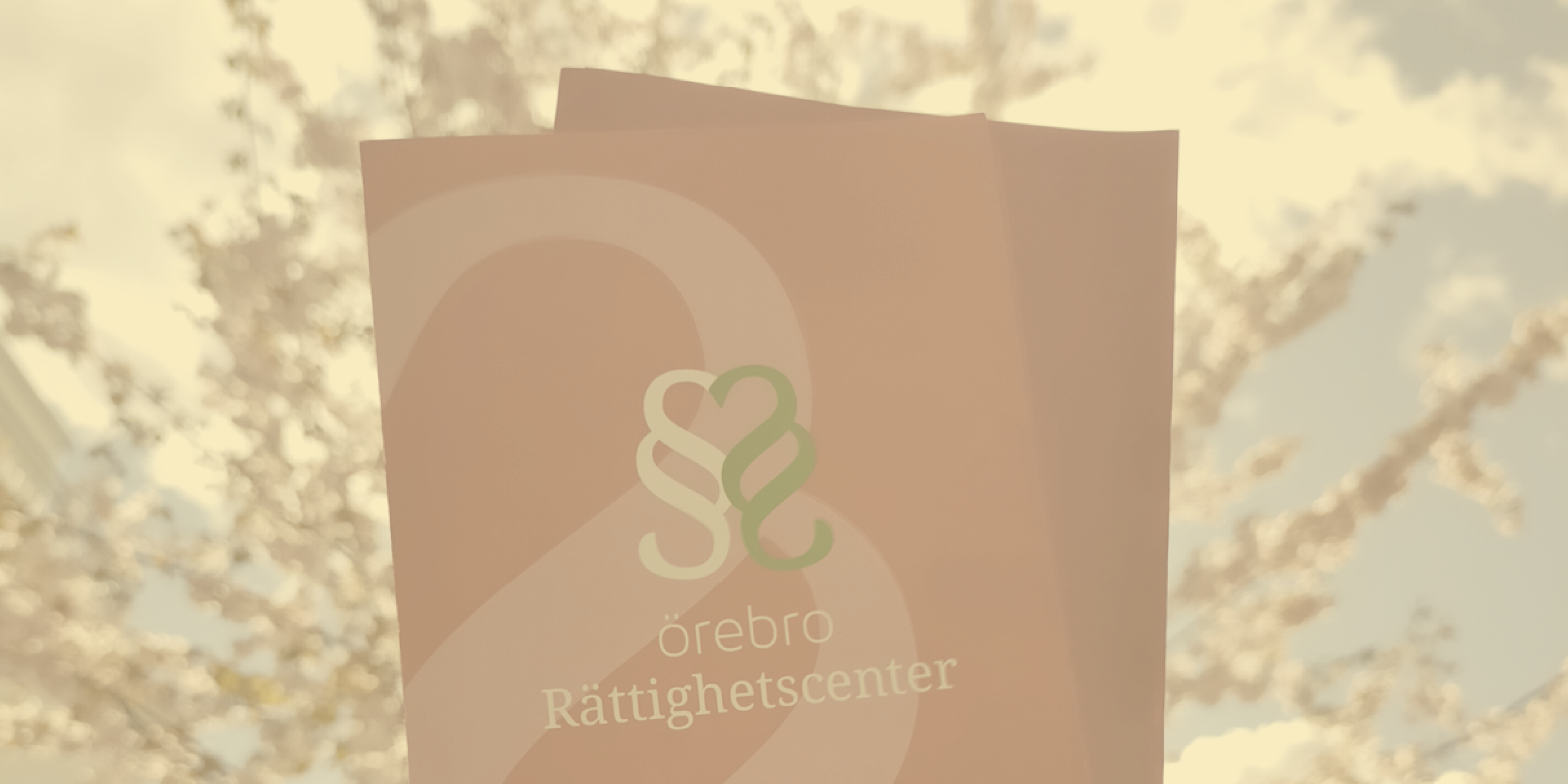 Foldrar med Örebro Rättighetscenters logga mot en bakgrund med blomstrande träd.